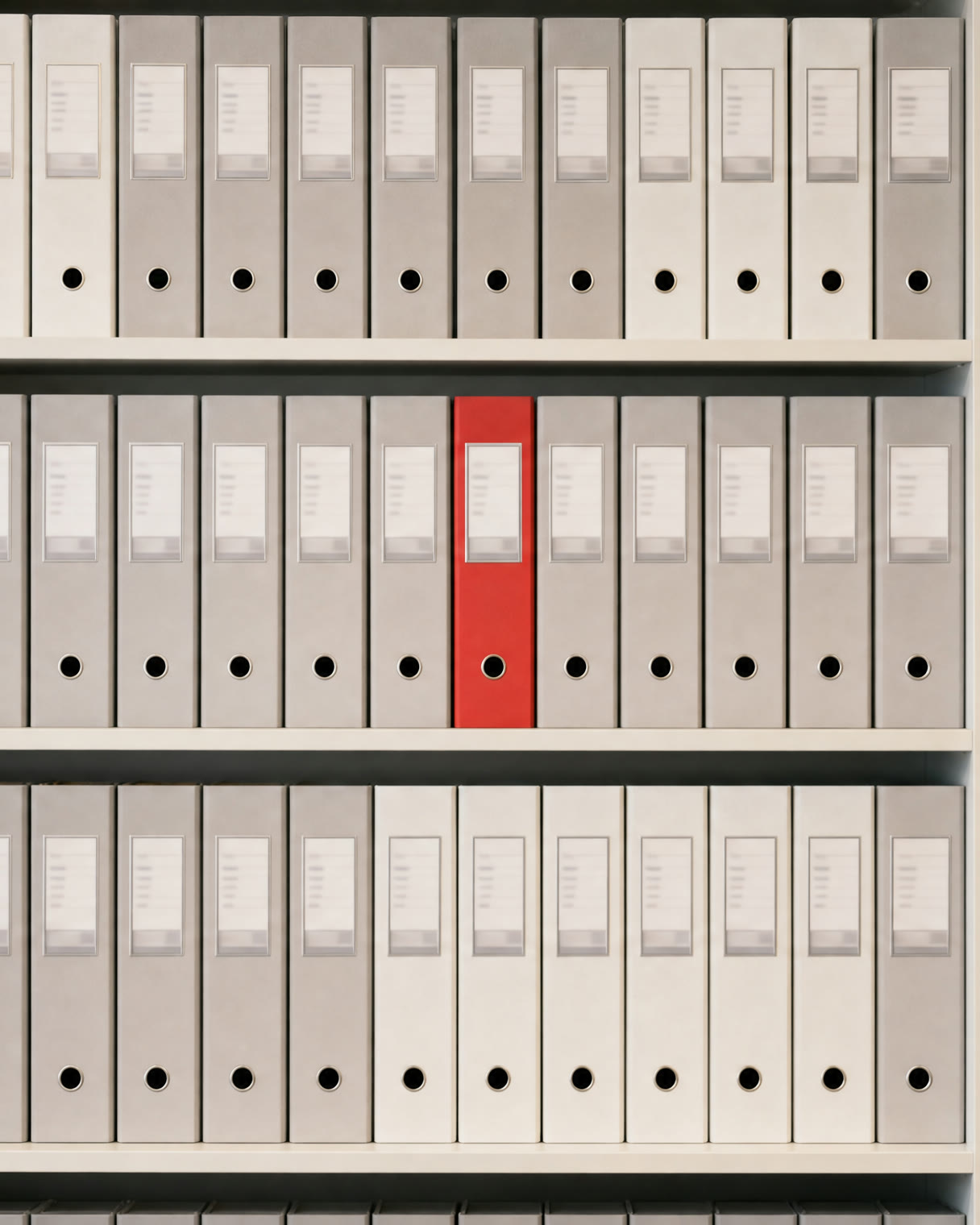 Shelves of identical grey company files in exact rows, one file bound in vermillion red, every spine squared and in its place